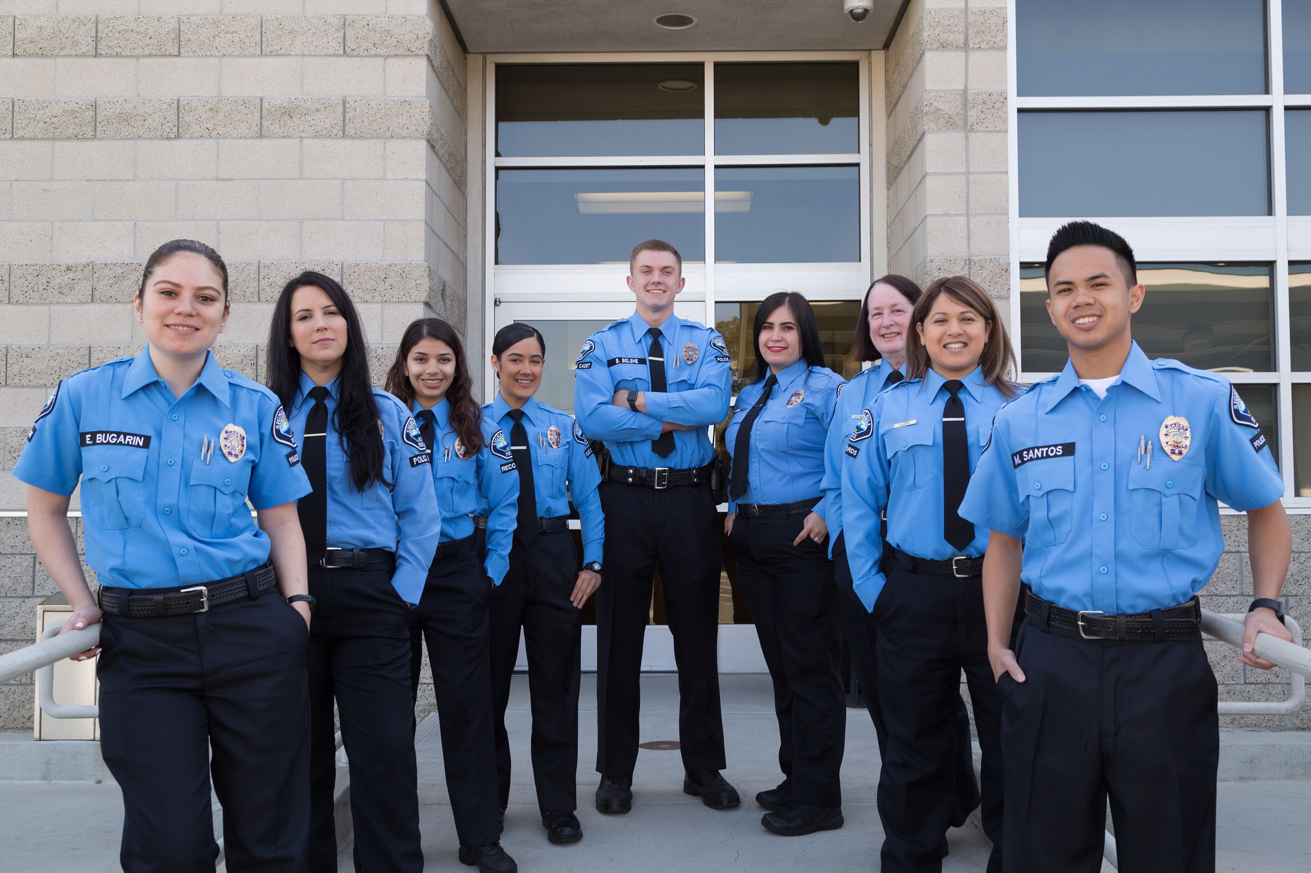 Group of police officers in blue uniforms smiling outside the department